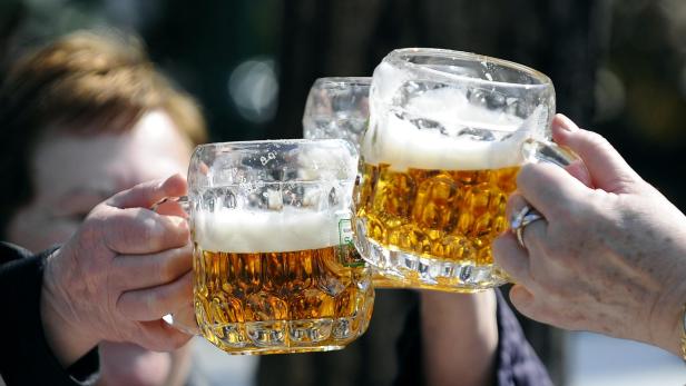 Eine Gruppe an Menschen stoßen mit halbvollen Bierkrügen an.