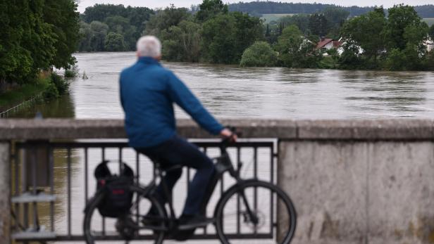 Radfahrer beobachtet auf Brücke hochwasserführenden Fluss