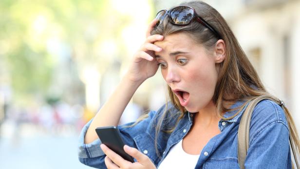 Frau schaut erschrocken auf ihr Handy