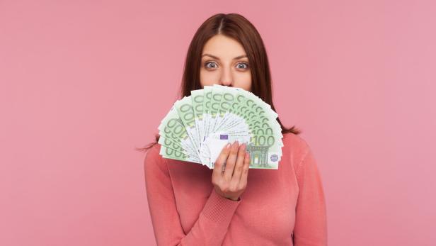 Amazed happy woman with brown hair in pink sweater hiding face behind fan of euro banknotes, interest-free cash withdrawal